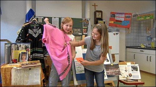 Sophie und Jule präsentieren ihren Mitschülern die Mode der 70er und 80er Jahre. »Das lustige ist, da ist eine Hose darunter. Die hat man angezogen, dann ist man so aus dem Haus gegangen, hat sich irgendwo im Busch oder so versteckt und hat die Hose ausgezogen und ist dann so in die Disco gegangen.«