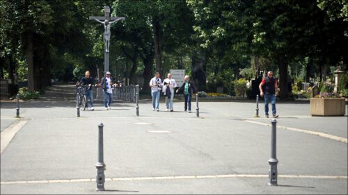 Einige Fussballfans auf dem Weg über den Friedhof in den Sportpark Ronhof, im Hintergrund ein großes Kreuz mit Jesusfigur, umgeben von Bäumen und Gräbern. Einige Fussballfans auf dem Weg über den Friedhof in den Sportpark Ronhof, im Hintergrund ein großes Kreuz mit Jesusfigur, umgeben von Bäumen und Gräbern.