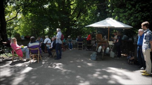 Sonntagnachmittag am Friedhofscafé: Ehrenamtliche stellen Kaffee und Kuchen bereit, Besucherinnen sitzen im Schatten und kommen miteinander ins Gespräch. Sonntagnachmittag am Friedhofscafé: Ehrenamtliche stellen Kaffee und Kuchen bereit, Besucherinnen sitzen im Schatten und kommen miteinander ins Gespräch.