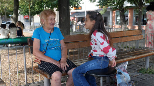 Eine alte Frau und ein Mädchen scherzen im Schatten der Bäume am Spielplatz. Dass sie verschieden Sprachen sprechen, bedeutet für die ungleichen Freundinnen keine Barriere. Eine alte Frau und ein Mädchen scherzen im Schatten der Bäume am Spielplatz. Dass sie verschieden Sprachen sprechen, bedeutet für die ungleichen Freundinnen keine Barriere.