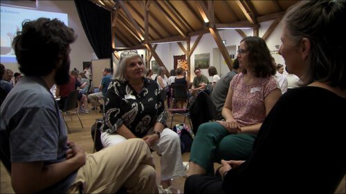 Mehrere Erwachsene sitzen im Stuhlkreis und unterhalten sich, im Hintergrund eine Projektion mit der Aufschrift "Sprechen & Zuhören" – Szene von einer Sprechen & Zuhören-Fortbildung.